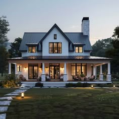 a large white house with lots of windows and lights on the front porch, surrounded by grass