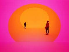 two people standing in front of an orange and pink background with the sun behind them