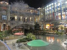 an outdoor patio with tables and umbrellas next to a pond in the middle of town