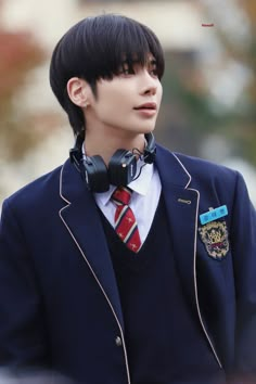 a young man with black hair wearing a suit and headphones on his ears, looking off to the side