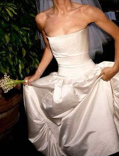 a woman in a white wedding dress standing next to a potted plant