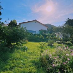 the sun shines brightly in front of a white house and lush green yard with pink flowers