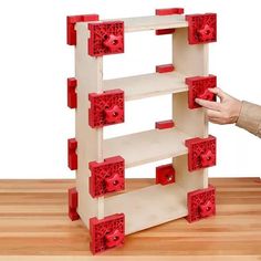 a wooden toy with red plastic parts on it's sides and two hands reaching for the blocks