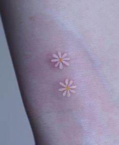 two small white flowers on the side of a woman's arm, both with yellow centers