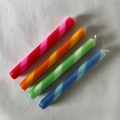 four brightly colored candles are lined up on a white surface, with one candle in the middle