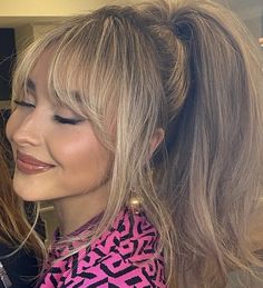 a woman with blonde hair wearing a pink shirt and gold earrings smiling at the camera