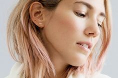 a woman with pink hair and ear piercings on her ears is looking to the side