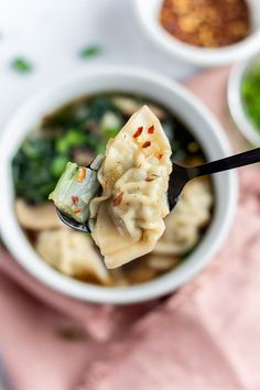 a spoon full of dumplings with broccoli and other foods in the background