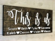 this is us wood sign with hearts and names in white on a wooden plank wall