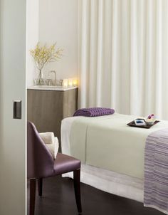 a white bed sitting next to a purple chair in a bedroom under a large window