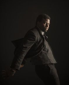 a man in a black suit and tie posing for a photo with his hands on his hips