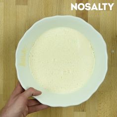 a person holding a white bowl with liquid in it on top of a wooden table