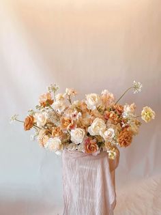 a vase filled with lots of flowers sitting on top of a white table covered in fur