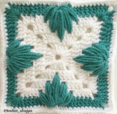 a crocheted square with green leaves on the center and white petals in the middle