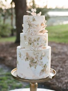 a three tiered wedding cake with flowers on the top is sitting on a gold stand