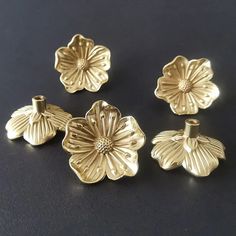 four pieces of gold metal sitting on a black surface with one flower in the middle