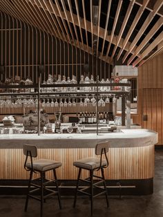 two bar stools sit in front of an empty bar with bottles on the shelves