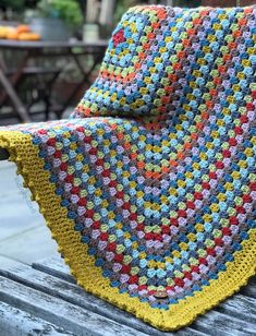 a crocheted blanket sitting on top of a wooden bench next to a table