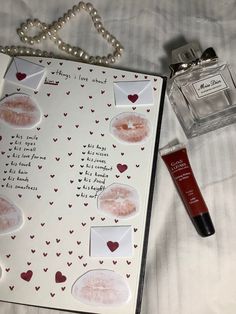 an open notebook with stickers on it next to a bottle of lipstick and a necklace