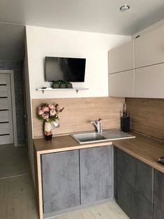 a kitchen with grey and white cabinets, a tv on the wall above the sink