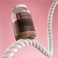 a jar of chocolate sitting on top of a white rope next to a pink background