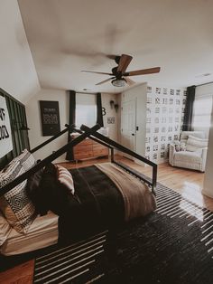 a bedroom with black and white bedding, wooden flooring and ceiling fan in the corner