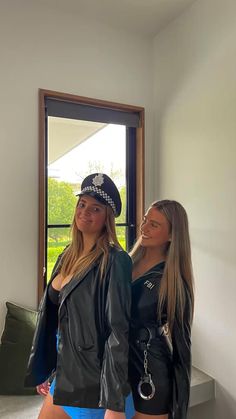 two beautiful young women standing next to each other in front of a window wearing police uniforms