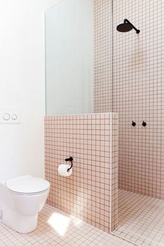 a white toilet sitting inside of a bathroom next to a walk in shower and tiled walls