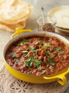 a yellow pot filled with chili next to some pita bread on a wooden table