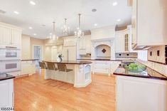 a large kitchen with white cabinets and an island in the middle of the room is lit by two chandeliers