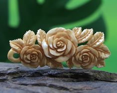 three carved roses are sitting on a piece of wood, ready to be used as brooches