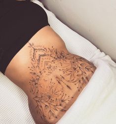 a woman laying on top of a bed with her stomach covered in tattoos and flowers