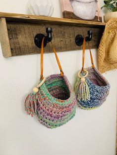 two crocheted purses hanging from hooks on a wooden shelf next to a hat rack