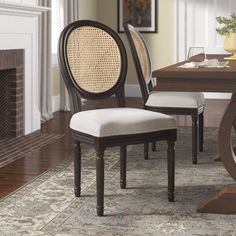 a dining room table with two chairs and a fire place in the background on a rug