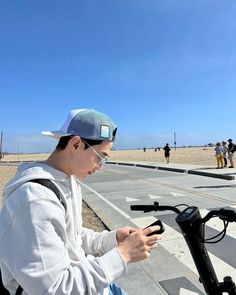 a young man sitting on top of a bike next to the beach while looking at his cell phone