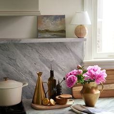 pink flowers in a vase on a kitchen counter next to a potted plant and other items