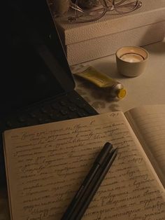 an open notebook sitting on top of a desk next to a laptop computer and cup of coffee