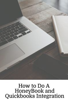 an open laptop computer sitting on top of a wooden table next to a notebook and cell phone