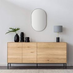 a wooden dresser with two vases and a round mirror on the wall above it