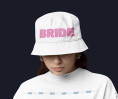 Bride Bucket Hat, Bach Bucket Hat, Honeymoon Outfit, Bride Sun Hat Introducing our stylish Bride Bucket Hat, the perfect accessory for your special celebrations! This chic white sun hat features playful pink checkboard writing that proudly declares "Bride," making it an ideal choice for bachelorette parties, honeymoon adventures, or simply soaking up the sun in style. Crafted for comfort and flair, this bachelorette hat is a must-have for any bride-to-be. Whether you're traveling for your honeymoon or enjoying a fun day with your bridal squad, this custom hat adds a touch of personality to your honeymoon outfit. It's not just a hat; it's a celebration of your love story. Make your bachelorette party unforgettable with this fashionable Bach bucket hat. Embrace the excitement of your upcomin White Sun Hat, Bachelorette Hats, Adventurous Honeymoon, Bridal Squad, Stylish Bride, Honeymoon Outfits, Bachelorette Parties, Bucket Hats, Custom Hats