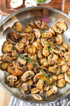 a pan filled with mushrooms and herbs on top of a wooden table