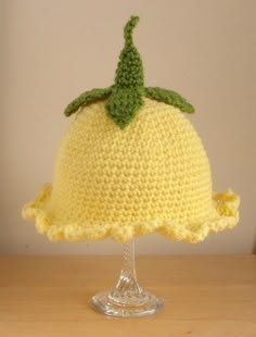 a crocheted yellow hat with a green leaf on top sitting on a table