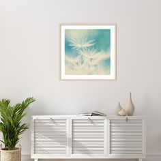 a white cabinet sitting next to a potted plant in front of a painting on the wall