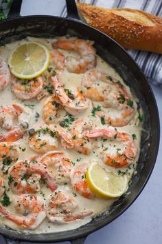 a skillet filled with shrimp and sauce next to a loaf of baguette bread