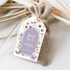 a tag that says thank you with purple flowers and butterflies on it, sitting next to some dried grass