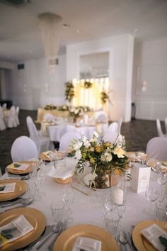 the table is set with white linens and gold plates, silverware, and flowers