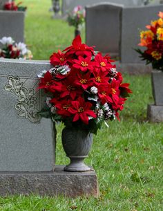 red flowers in a vase sitting on top of a headstone next to other headstones