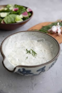 a close up of a bowl of soup on a table with salad in the background