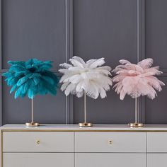 three different colored ostrich feathers sitting on top of a white dresser next to a gray wall