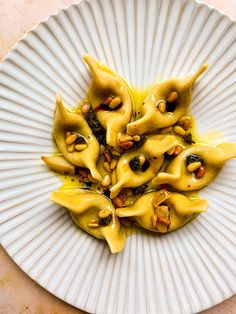 a white plate topped with dumplings covered in sauce and nuts on top of a table